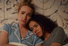ginny and georgia lay on a bed with their arms folded, looking at each other