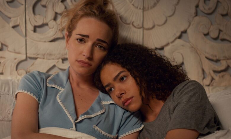 ginny and georgia lay on a bed with their arms folded, looking at each other